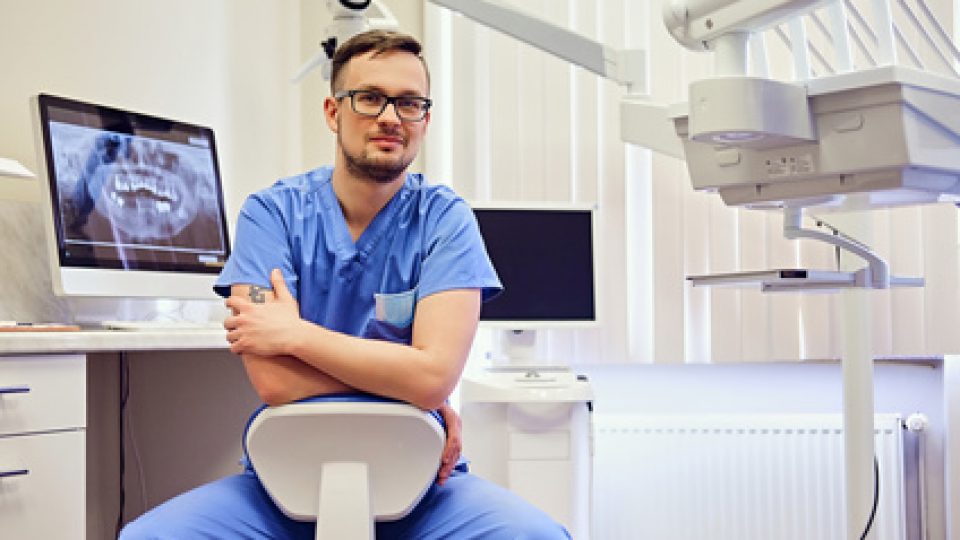 Male dentist in a room with medical equipment on background.